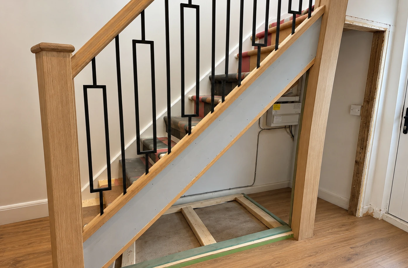 Before visualisation: exposed under-stairs space beneath an oak staircase with black metal balusters.